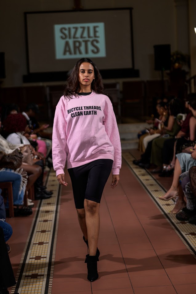 A model walking the runway at a Sizzle Arts fashion show wearing a sustainability-themed design